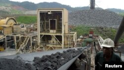 FILE - A worker at Ashanti Goldfield Company's big mine in Obuasi, Ghana, walks next to a conveyor belt carrying ore up to a processing plant, Oct. 23, 2003.