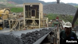 FILE - A worker at Ashanti Goldfield Company's big mine in Obuasi, Ghana, walks next to a conveyor belt carrying ore up to a processing plant, October 23, 2003.