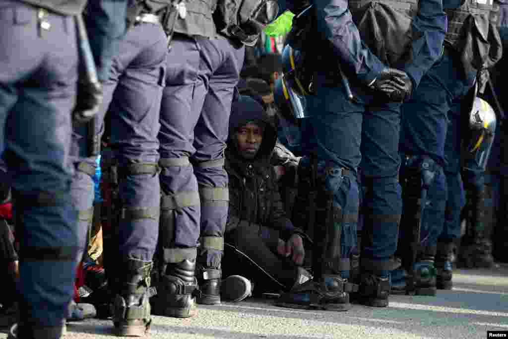 French police stand near as migrants wait in front of a processing center to be registered on the second day of their evacuation and transfer to reception centers in France, during the dismantlement of the camp called "the jungle" in Calais, France, Oct. 