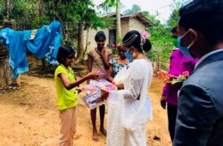 Pawani Rasanga hands a packet to a young girl, watched by her husband Darshana Kumara Wijenarayana in the small town of Malimbada, about 160 kilometers (99 miles), south of the capital Colombo.