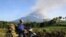 An Indonesian man carrying firewood on a motorcycle passes a field in Banyuwangi located in eastern Java island as Mount Raung volcano emits steam and ash (background), July 21, 2015.