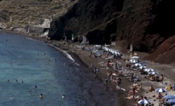 FILE - Tourists sunbathe on the Red Beach on the Greek island of Santorini, Greece, July 2, 2015.