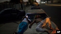 Andres Quintero, left, and Fermin Perez rest on top of Perez's car as they wait in line for over 20 hours to fill their tanks with gas in Cabimas, Venezuela, May 16, 2019. 