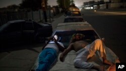 Andres Quintero, left, and Fermin Perez rest on top of Perez's car as they wait in line for over 20 hours to fill their tanks with gas in Cabimas, Venezuela, May 16, 2019. 