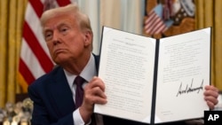 President Donald Trump holds up a signed executive order relating to AI in the Oval Office of the White House, Jan. 23, 2025, in Washington. 