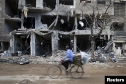 A man rides a bicycle near damaged buildings in Jobar, a suburb of Damascus, Syria, Oct. 27, 2015.