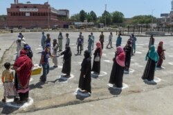 People stand in designated areas marked on the ground to maintain social distanciation as they receive free food from volunteers in Karachi on March 27, 2020.