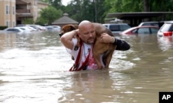 FILE - Louis Marquez carries his dog Dallas through floodwaters after rescuing the dog from his flooded apartment in Houston.