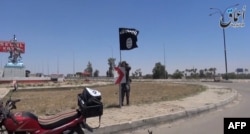 An image taken from a video uploaded on May 18, 2015 by Aamaq News Agency, a Youtube channel which posts videos from areas under the Islamic State (IS) group's control, allegedly shows an IS fighter hanging a flag of the group in a street of Ramadi, the I