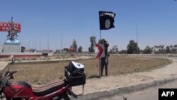 FILE - An image taken from video uploaded Aamaq News Agency, a YouTube channel which posts videos from areas under the Islamic State group's control, allegedly shows an IS fighter hanging a flag of the group in a street of Ramadi, Iraq.
