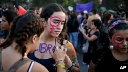 FILE - A woman writes the word "Free" on her friend at an event marking International Women's Day in Santiago, Chile.