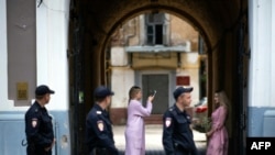 Beberapa polisi yang sedang berpatroli melintas di depan dua perempuan Rusia yang saling berfoto di depan pintu masuk, di Kota Nizhny Novgorod, Rusia yang sedang berlangsung turnamen sepak bola Piala Dunia 2018, 21 Juni 2018.