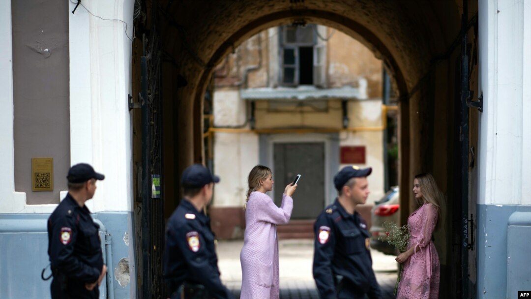 Beberapa polisi yang sedang berpatroli melintas di depan dua perempuan Rusia yang saling berfoto di depan pintu masuk, di Kota Nizhny Novgorod, Rusia yang sedang berlangsung turnamen sepak bola Piala Dunia 2018, 21 Juni 2018.