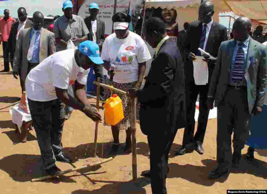 South Sudanese Vice President Wani Igga (centre, in suit) watches as a volunteer demonstrates how to wash hands with water from a jerry can. 