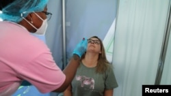 A healthcare worker collects a swab from Bronwen Cook for a PCR test against the coronavirus disease (COVID-19) before traveling to London, at O.R. Tambo International Airport in Johannesburg, South Africa, Nov. 26, 2021. 