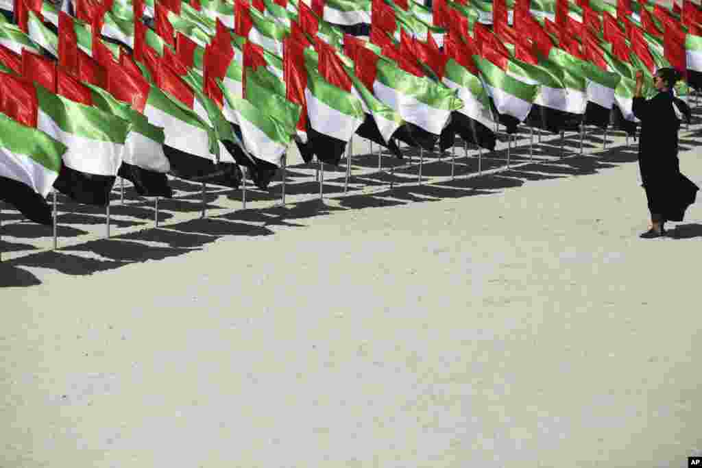 A woman takes a photograph of a display of Emirati flags set up for National Day in Dubai, United Arab Emirates.