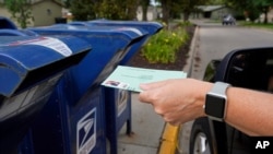 FILE - In this Aug. 18, 2020, photo, a person drops applications for mail-in-ballots into a mailbox in Omaha, Neb. The U.S. Postal Service agreed Wednesday, Oct. 14, to reverse changes that slowed mail service nationwide, settling a lawsuit.