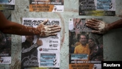 Opposition supporters use their hands to glue posters of candidates for the National Assembly of the Venezuelan coalition from opposition parties (MUD) in Caracas, Dec. 2, 2015.