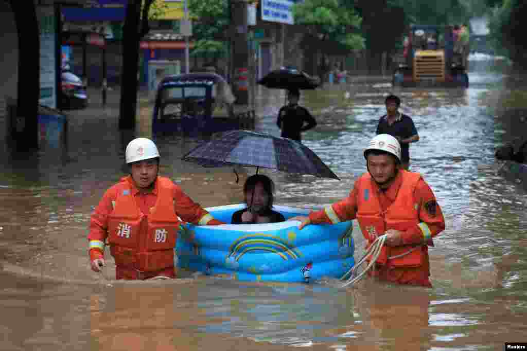 Rescue workers evacuate a woman with an inflatable swimming pool on a street following heavy rainfall in Pingxiang, Jiangxi province, China, July 9, 2019.