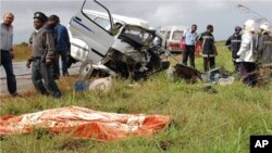 Vítimas de acidente numa estrada moçambicana jazem, cobertos com manta cor de laranja, junto aos destroços dos veículos.