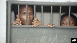 Two prisoners peer through the bars of their cell in Mogadishu on Friday, Jan. 29, 1993 at the former Criminal Investigation Division, the department that probed so-called political crimes.