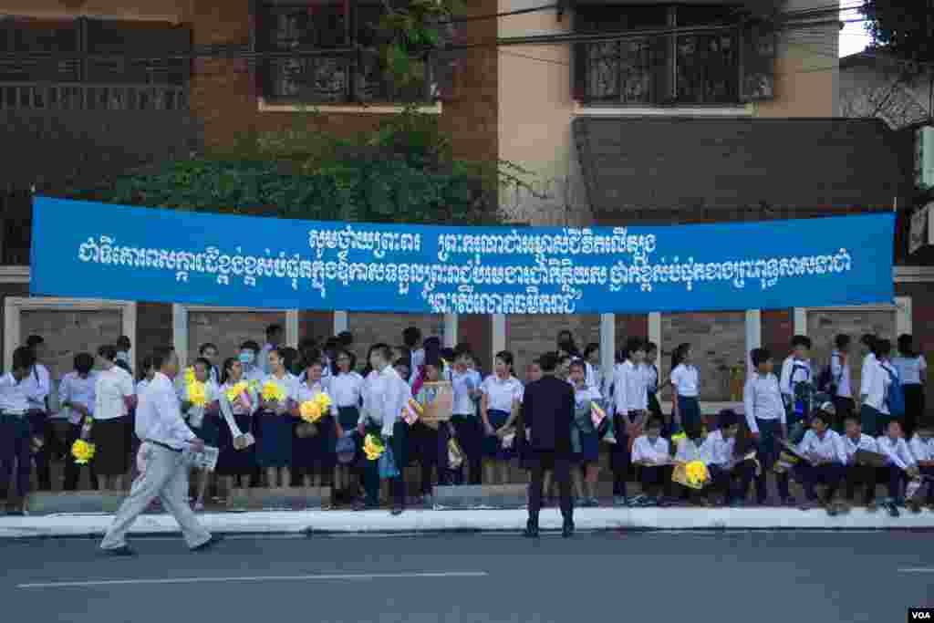 Students are waiting on the pavement under the banner with text honoring the title &quot;Preah Sri Loka Dhammika Raja&quot; to King Norodom Sihamoni on June 3, 2015. (Nov Povleakhena/VOA Khmer)