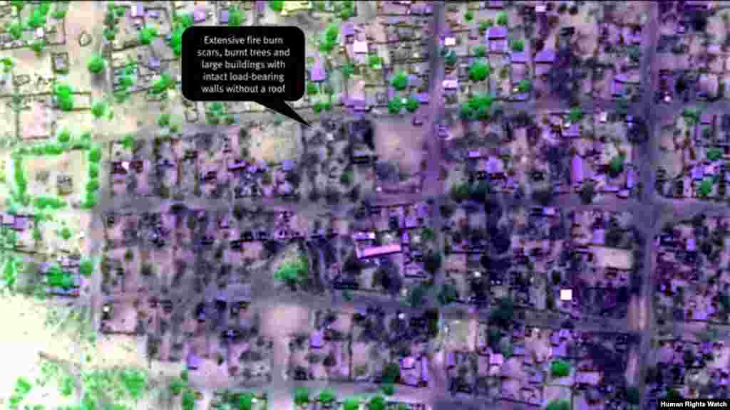 Post-violence view of concentration of building damages (view 3). Extensive fire burn scars, burnt trees and large buildings with intact load-bearing walls without a roof are seen.