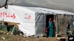 FILE - A woman stands outside her tent in a Syrian refugee camp in Houch al-Harimeh, Lebanon. Refugees in Syria’s neighboring countries often live in terrible conditions, spurring many to attempt the journey to Europe.