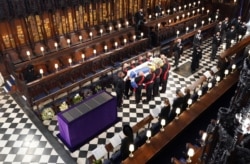 Queen Elizabeth II watches as pallbearers carry the coffin of Britain's Prince Philip during his funeral at St. George's Chapel, at Windsor Castle, in Windsor, Britain, April 17, 2021.