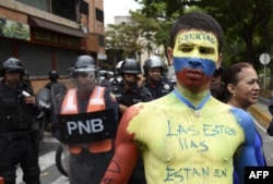 Un hombre con su cuerpo pintado con los colores de la bandera nacional venezolana se manifiesta frente a la policía antidisturbios durante una manifestación de la oposición que pide a las fuerzas armadas que desobedezcan al presidente en disputa de Venezuela Nicolás Maduro, cerca de la base aérea de La Carlota en Caracas. Mayo 4 de 2019.