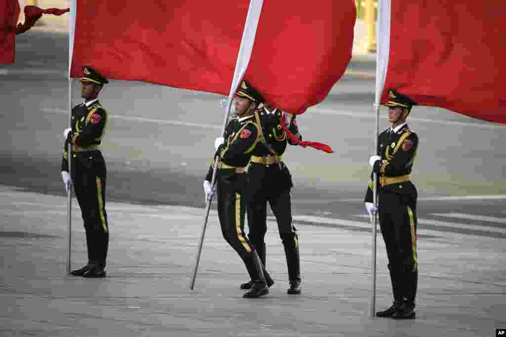 یک عضو ارتش چین، پرچم سرخی را در دست دارد و همزمان تعادلش بخاطر باد شدید بهم خورده است.