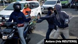 Para pedagang kaki lima menawarkan sarung tangan kepada para pengendara motor di sebuah pos pemeriksaan di tengah pemberlakuan Pembatasan Sosial Berskala Besar untuk mencegah penyebaran virus corona (Covid-19) di Makassar, Sulawesi Selatan, 6 Mei 2020. (F