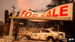 Znak za prodaju kod kuće dok automobili tinjaju tokom požara u Eatonu u oblasti Altadena u okrugu Los Angeles, Kalifornija, 8. januara 2025.