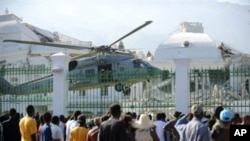 Haitians watch as a US Navy helicopter lands in front of the heavily damaged presidential palace in Port-au-Prince 19 Jan 2010