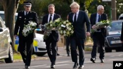 British Prime Minister Boris Johnson and leader of the Labour Party Keir Starmer, second from left, carry flowers as they arrive at the scene where member of parliament David Amess was stabbed Friday, in Leigh-on-Sea, Essex, England, Oct. 16, 2021. 