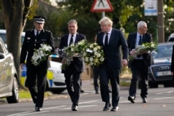 British Prime Minister Boris Johnson and leader of the Labour Party Keir Starmer, second from left, carry flowers as they arrive at the scene where member of parliament David Amess was stabbed Friday, in Leigh-on-Sea, Essex, England, Oct. 16, 2021.