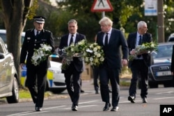 British Prime Minister Boris Johnson and leader of the Labour Party Keir Starmer, second from left, carry flowers as they arrive at the scene where member of parliament David Amess was stabbed Friday, in Leigh-on-Sea, Essex, England, Oct. 16, 2021.