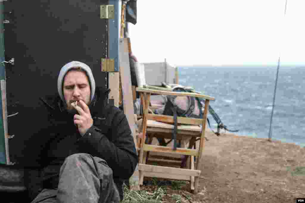 A volunteer has a quick cigarette on Lesvos, Greece. Those on watch for migrants sailing from Turkey check the ocean with binoculars every 15 minutes. (J. Owens/VOA)