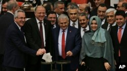 Turkish Prime Minister Binali Yildirim, center, and lawmakers cast their votes during Turkey's parliamentary debate proposing constitutional amendments that would hand President Recep Tayyip Erdogan's largely ceremonial presidency sweeping executive powers, in Ankara, Turkey, Jan. 21, 2017.