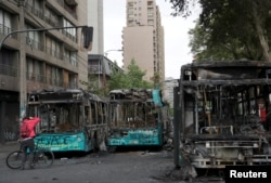 Un hombre toma fotos de autobuses calcinados en Santiago la víspera durante protestas contra el alza de precio de los boletos de metro Foto Reuters, Iván Alvarado. Domingo 20 de octubre de 2019