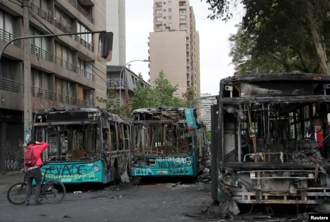 Un hombre toma fotos de autobuses calcinados en Santiago la víspera durante protestas contra el alza de precio de los boletos de metro Foto Reuters, Iván Alvarado. Domingo 20 de octubre de 2019