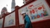 资料照：建筑工人走过北京一个居民小区外面，墙上有宣传牌《社会主义核心价值观：富强》《社会主义核心价值观：民主》（2016年12月13日）