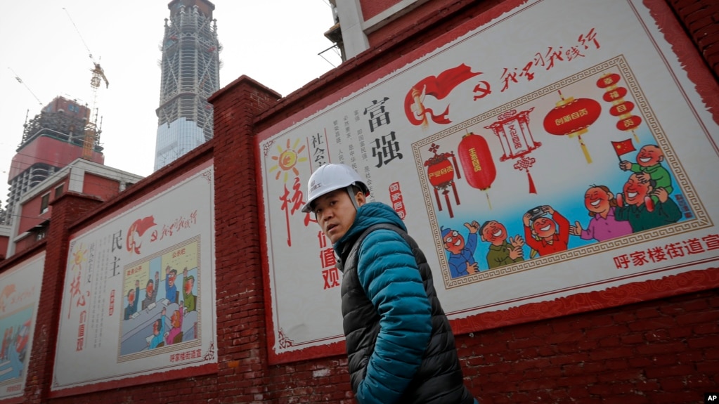 资料照：建筑工人走过北京一个居民小区外面，墙上有宣传牌《社会主义核心价值观：富强》《社会主义核心价值观：民主》（2016年12月13日）(photo:VOA)