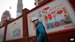 资料照：建筑工人走过北京一个居民小区外面，墙上有宣传牌《社会主义核心价值观：富强》《社会主义核心价值观：民主》（2016年12月13日）
