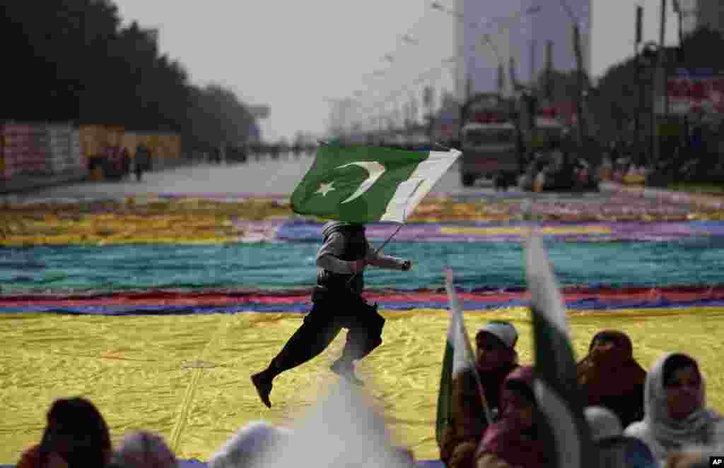 Supporters of Pakistani Sunni Muslim cleric Tahir-ul-Qadri listen to speeches while awaiting his arrival in Islamabad, as a youth runs across the street holding a national flag. 