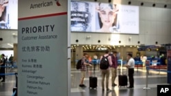 In this July 6, 2018, photo, travelers stand near a signboard at the American Airlines check-in counters at the Beijing Capital International Airport in Beijing. (AP Photo/Mark Schiefelbein)
