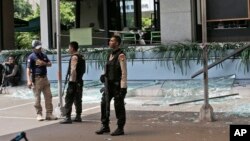 Police officers stand guard outside a damaged Starbucks cafe after an attack in Jakarta, Indonesia Thursday, Jan. 14, 2016.