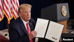 El presidente Donald Trump muestra a las cámaras una de las órdenes ejecutivas para asistencia federal por el coronavirus firmadas el sábado 8 de agosto de 2020.