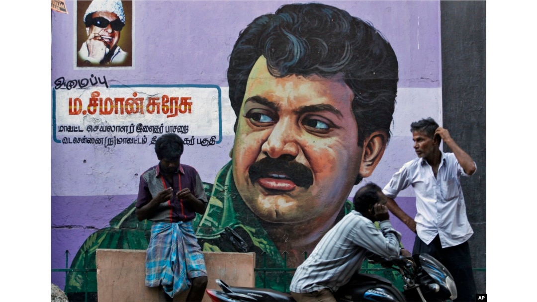 FILE - People stand in front of a mural of Sri Lanka's Liberation Tigers of Tamil Eelam (LTTE) leader Velupillai Prabhakaran painted on a wall in Chennai, India, May 19, 2015. Across Chennai, large billboards with photographs of Prabhakaran, the leader of the Tamil Tigers, urge its people to "not forget" the day the insurgent group accepted defeat.