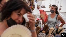 FILE - Women cool themselves with fans in the Rastro flea market during a heatwave in Madrid, Spain, Aug. 15, 2021. (AP Photo/Andrea Comas, file)